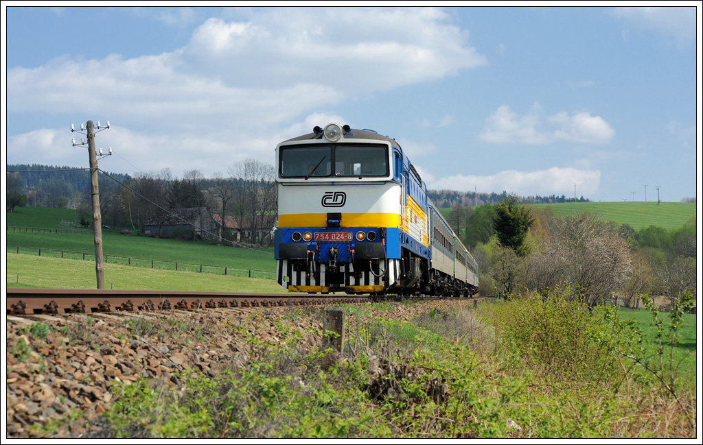 754 024 bespannte am 17.5.2011 bis Klatovy (deutsch Klattau) den R 827 von Bayerisch Eisenstein nach Praha hl.n. (Prag). Ab Klatovy bernimmt dann eine E-Lok diesen Zug. Die Aufnahme entstand vor Desenice (deutsch Deschenitz).