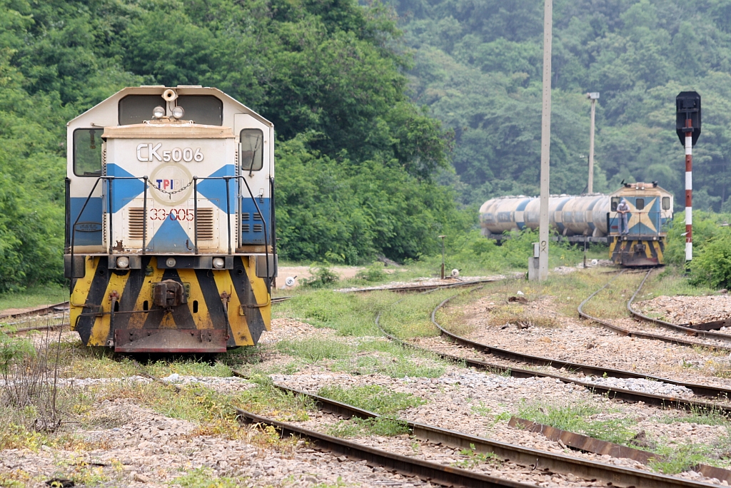 Während die TPIPL 33-005 (ex CK5 006) eine Pause hält, nähert sich im Hintergrund auf der Anschlußbahn die TPIPL 33-003 (ex CK5 004) mit einem Zementwagenzug der Hin Lap Station; aufgenommen am 23.August 2010.