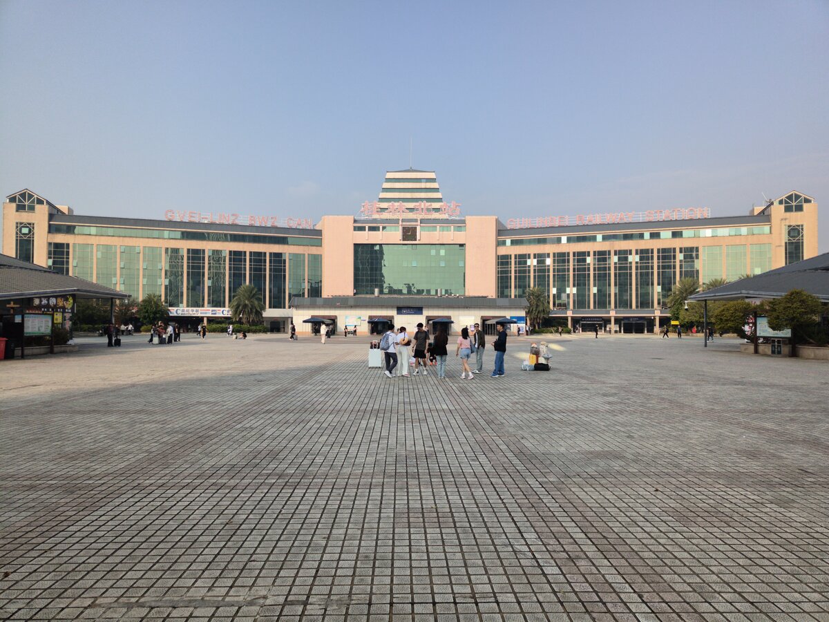 2024.11.15, Station Front Plaza, GuiLin North Station. You might notice apart from regular PuTonghua PinYin spelling of GuiLin Bei (North), theres another line saying Gveilinz Bwz Can. This was written in Vahcuengh, language of the Zhuang Ethnic. Being the largest group of minor ethnic with around 1/6 to 1/5 population of Germans, Zhuang proudly took the GuangXi Autonomous Prov. and, as GuiLin was the old capital of GuangXi Prov., both factor resulted as a rare moment where non-PuTongHua Station Name was used.
///
2024.11.15, Station Front Plaza, GuiLin Nordbahnhof. Vielleicht fällt Ihnen auf, dass neben der regulären PuTonghua PinYin-Schreibweise von GuiLin Bei (Nord) eine weitere Zeile mit Gveilinz Bwz Can steht. Dies wurde in Vahcuengh geschrieben, der Sprache der ethnischen Gruppe der Zhuang. Da die Zhuang mit etwa 1/6 bis 1/5 der deutschen Bevölkerung die größte ethnische Minderheit sind, nahmen sie stolz die autonome Provinz GuangXi ein, und da GuiLin die alte Hauptstadt der Provinz GuangXi war, führten beide Faktoren zu einem seltenen Moment, in dem ein nicht-PuTongHua-Stationsname verwendet wurde.