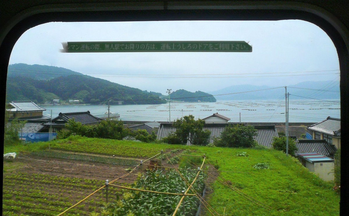 Ôfunato-Linie: Nachdem der Tsunami hier alles weggerissen hat und von dieser schönen Landschaft nur noch eine Schlammwüste übrig ist lässt sich ein solches Bild nicht mehr machen. Aufnahme durch die Ausstiegstüre des Triebwagens KIHA 100-42 vor Otomo. Der Streifen an der Türe liest  Bei Einmannbetrieb an den unbedienten Stationen beim Fahrer ausstiegen . 9.Juli 2010. 