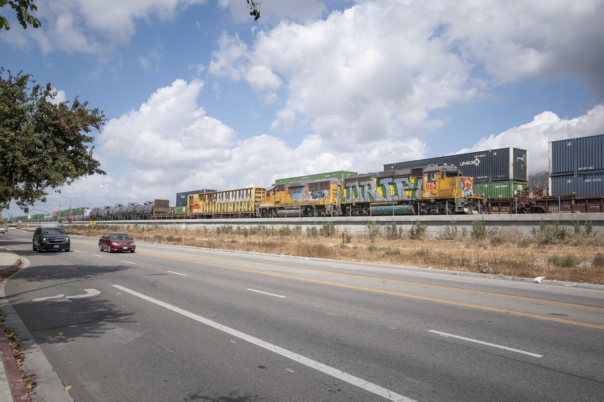 Am 16.09.2024 kam 1162 (GP60s) von Union Pacific mit einem Nahgüterzug aus Richtung Santa Clarita nach Burbank (USA-Kalifornien). Dahinter ein Containerzug wartend in die Gegenrichtung. 

(Graffiti: Ich kann es verstehen, welcher Sinn dahinter steckt, aber.... dann müssten erst einmal eure Regeln überarbeitet werden. Andersherum ist es bei einer andere GP0 durch gegangen und bei den Amerikanern und dem hippen Los Angeles nahe zu typisch, wobei die Baureihe die einzige ist, die es erwischt hat.  Mit den Schrägen nehme ich hin, aber auch dabei kommt es drauf an mit welchem Objektiv man arbeitet. In diesem Fall ist es ein Weitwinkel und auch bei Brennweite 20mm hat es leider seine Schwäche. )