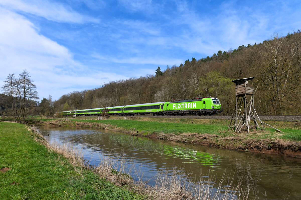 Am 31. März 2024 bespannte die im Flixtrain-Design gehaltene 193 940 der ELL den FLX 1243 nach Stuttgart HBF. Zwischen Neukirchen und Hünfeld passierte sie einen idyllisch gelegenen Jägerstand am Ufer der Haune. In den letzten Monaten gab es bei der Bespannung der Züge auf dieser Destination einen Generationenwechsel, die Loks der Baureihe 182 wurden durch Vectrons abgelöst. Die hier gezeigte 193 940 wurde 2023 ausgeliefert und war bisher schon für die Wiener Lokalbahnen Cargo und für DB Regio im Einsatz. Interessant ist die Tatsache, dass man eine Lok mit Mehrsystemausrüstung für den Einsatz vor dem rein innerdeutsch verkehrenden Flixtrain einsetzt. 