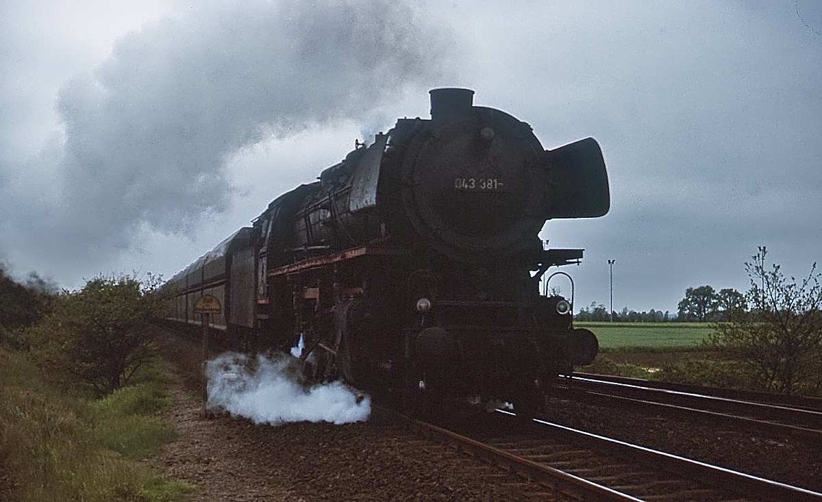 An einem trüben Frühjahrswochenende 1975 dampft die 043 381-3 bei Lathen in Richtung Emden (ungefähre Positionsangabe). Die Lok wurde am 29.09.1941 von der Maschinenfabrik Esslingen (Fabrik-Nr. 4446) an die Reichsbahn geliefert und am 27.10.1977 als eine der letzten Dampfloks der DB ausgemustert. Heute ist sie im Besitz des Bayerischen Eisenbahnmuseums Nördlingen.