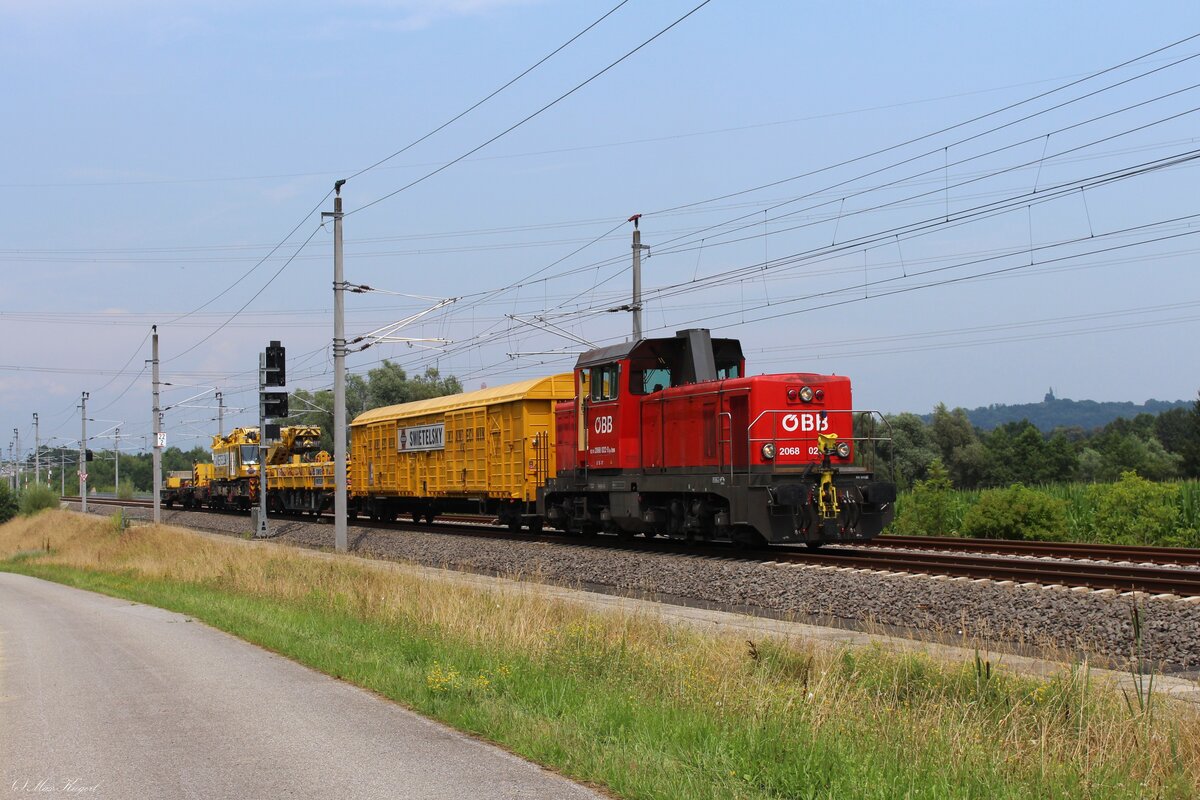 Auf der gut 10 Promille steilen Rampe von Werndorf zum Hengsbergtunnel fährt die 2068 022 als Arbeitszuglok am 10.7.2024 mit einem Kirow-Kran der Firma Swietelsky von Werndorf nach Wettmannstätten.