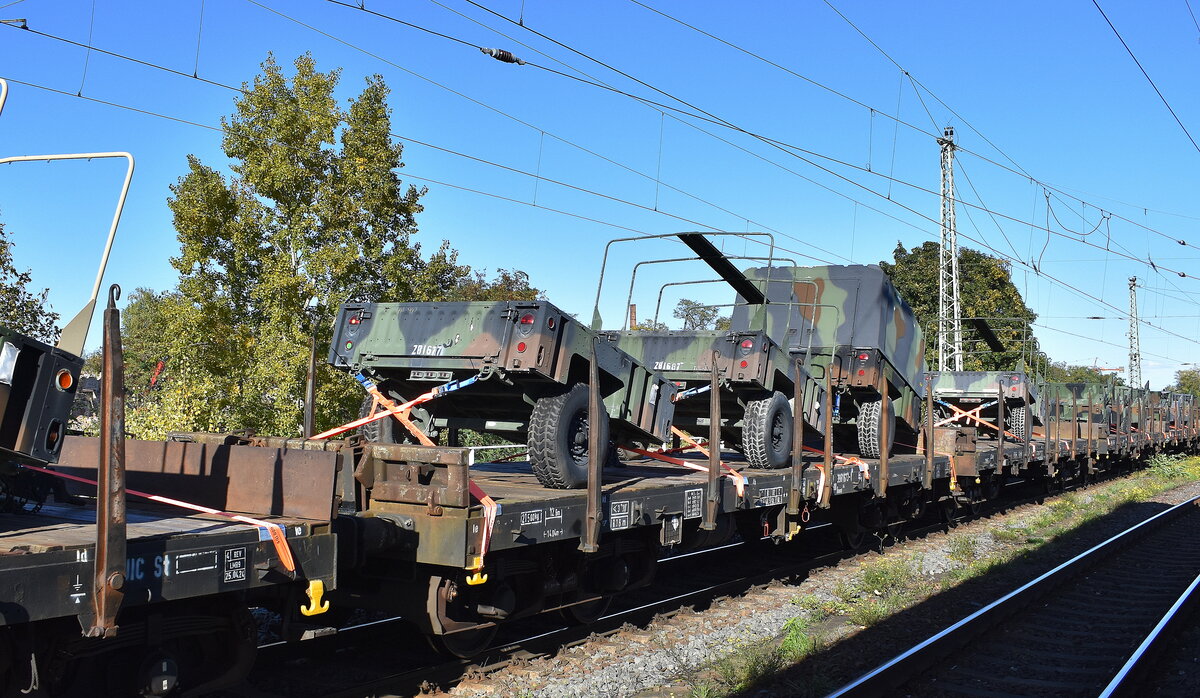 DB Cargo mit Drehgestellflachwagen mit vier Radsätzen, mit Stirnwandklappen, ohne Seitenborde und mit Rungen der Wagengattung Rmms 664, beladen mit einachsigen Militärhängern in einem Militärtransportzug am 15.10.24 Höhe Bahnhof Magdeburg Neustadt.