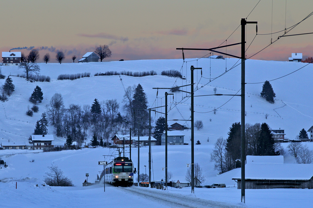 Der Voralpenexpress Triebzug der SOB,RBDe 561 083 taucht in der Abenddämmerung bei Schwyzerbrugg auf.Bild vom 9.2.2015 