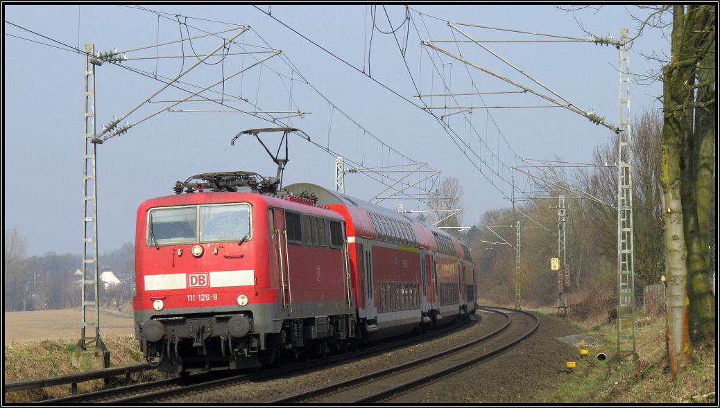 Die 111 126-9 ist mit dem Wupper Express (RE4) unterwegs nach Aachen. Hier zu sehen am BÜ bei Rimburg,unweit von Übach Palenberg, auf der Kbs 485 am 18.03.15.