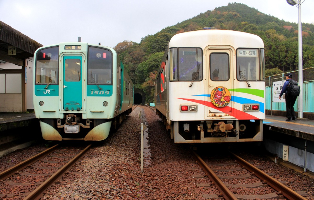 Die Asa Kaigan-Bahn: Im äussersten Südosten der Insel Shikoku am Pazifik befindet sich die unrentabelste Bahn Japans, die Bahn an der Küste (kaigan) von Asa. Diese Drittsektor-Bahn ist nur 8,5 km lang und hat die geringste Zahl von Fahrgästen unter den japanischen Privatbahnen. Die Stilllegung ist so gut wie sicher. Die Linie hätte Teil einer raschen Verbindung sein sollen zwischen den grossen Städten Tokushima und Kôchi um die weit in den Pazifik ragende Muroto-Halbinsel herum im Südosten von Shikoku. 1980 erfolgte ein Baustop. Da die 8,5 km von Kaifu nach Kannoura jedoch praktisch fertig waren, eröffnete man diesen Teil schliesslich 1992 als Asa Kaigan-Bahn. Die fehlenden 50,2 km (bis Nahari bei Kôchi) werden sicher nicht fertig erstellt. Bild: Links ist der Triebwagen 1509 von JR Shikoku (Mugi-Linie) in Kaifu eingetroffen, rechts steht Wagen 101 der Asa Kaigan-Bahn bereit für die Weiterfahrt nach Kannoura, 3.April 2015. 