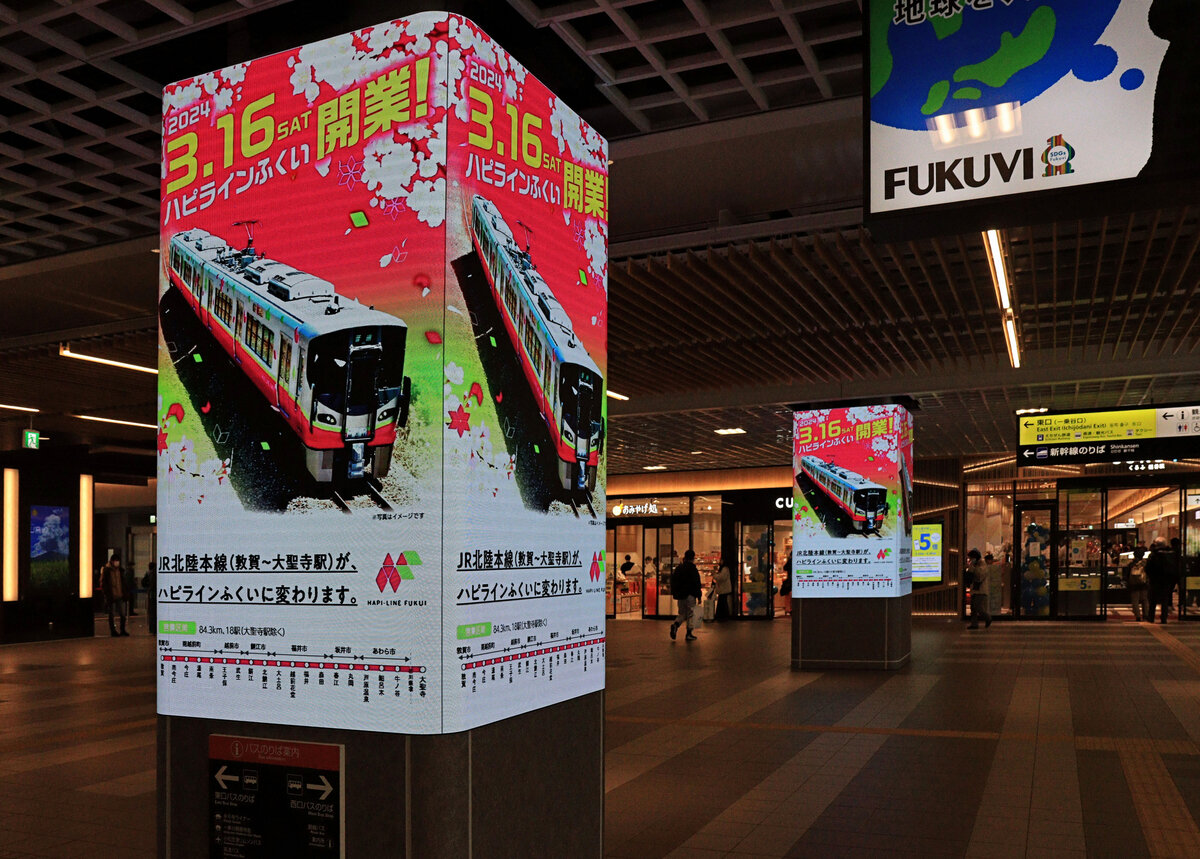 Die Hapi-Line Fukui: Nach der Eröffnung der neuen Hochgeschwindigkeitsstrecke Shinkansen von Kanazawa bis Tsuruga kam innerhalb der Praefektur Fukui die bisherige Hauptstrecke (Hokuriku Honsen) dem Japanischen Meer entlang in private bzw. lokale Hand. Jetzt betreibt hier seit dem 16.März 2024 die Hapi-Line Fukui eine Strecke von 84, 3 km, was auch den 13’870 Meter langen Hokuriku Tunnel umfasst. Von JR West Japan wurden 16 Züge Serie 521 für ihre Dienste übernommen. Der Name der Bahn wird zwar «hapi» geschrieben, verweist aber auf das englische Wort «happy», was wiederum auf den Städte- und Praefekturnamen «Fukui» hindeutet, mit dem Wortelement «fuku» = Glück. Das Bild zeigt den neuen Bahnhof Fukui mit grossen Werbetafeln für die erst 4 Tage zuvor eröffnete Hapi-Line Fukui. Die von JR West Japan übernommenen Züge sollen - wie im Bild - rosa gestrichen werden, mit hellgrünem Streifen. 19.März 2024 