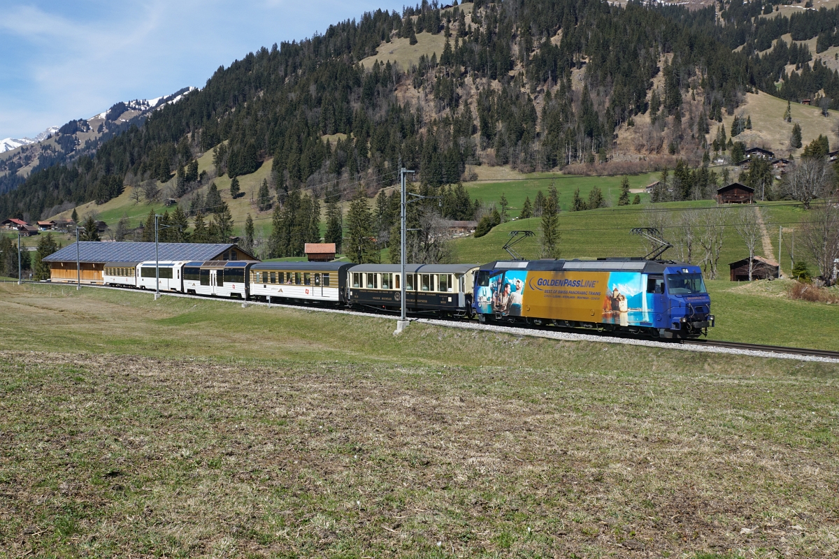 Ge 4/4 8004 befindet sich am 12.04.2015 mit einem Gemischtwarenladen bei Gruben.