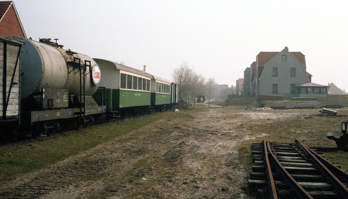 Inselbahn Spiekeroog__April 1984. Inselbahn GmP, zusammengestellt für den Abtransport : offene und gedeckte G-Wagen ex OEG, Heizöl-Kesselwagen 32 und die P-Wagen 12+13 ex MEG Zell-Todtnau, im (ehemaligen) Bahnhofsgelände.