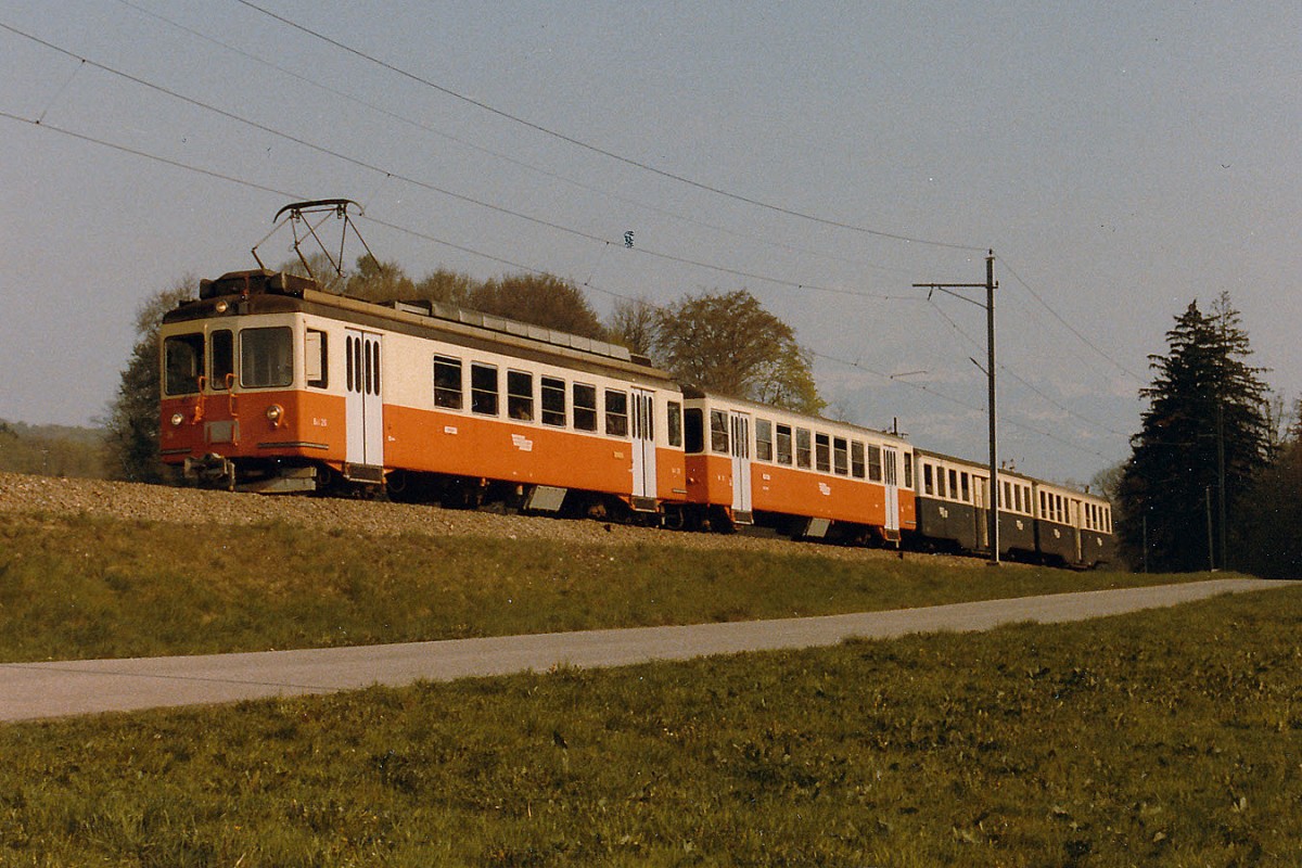 LEB: Bei der LEB handelt es sich um die erste Schmalspurbahn der Schweiz. Sie bedient den vorwiegend landwirtschaftlich bedeutenden  Gros de Vaud  und hat sich im Lauf der Jahre vom altmodischen Überlandbähnlein zum modernen Transportunternehmen entwickelt. Der Güterverkehr wurde im Jahre 1970 eingestellt. Die neusten LEB-Pendelzüge (Be 4/4 + Bt) wurde an Werktagen am späteren Nachmittag mit zwei alten Mitteleinstiegwagen verstärkt. Die Aufnahme vom Mai 1984 dokumentiert eine Fahrt nach Bercher. Die LEB beschaffte im Jahre 1966 die SWS/MFO Fahrzeuge gemeinsam mit der SZB, der OJB und der SNB. Bereits im Jahre 1970 hat die damalige BTI dieses Rollmaterial von der SZB übernommen und noch bis ca. 1998 im Personenverkehr eingesetzt. Zwei B-Wagen wurden nur für die LEB gebaut. Die beiden dreiteiligen LEB-Pendelzüge präsentierten sich mit dem traditionellen grün/cremen Anstrich (Be 4/4 25) sowie dem neuen orange/cremen Versuchsanstrich (Be 4/4 26).
Foto: Walter Ruetsch     