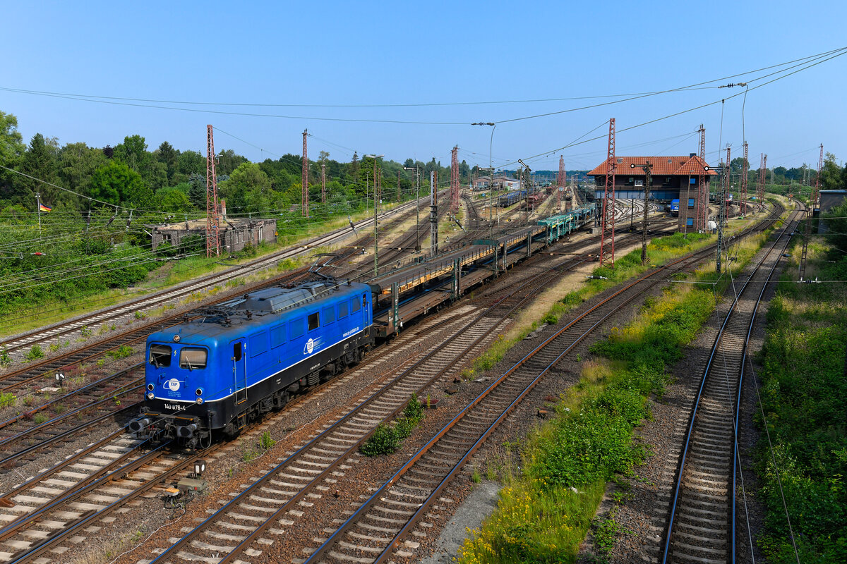 Nachdem am 27. Juni 2024 die E 40 002 mit ihrem Neuwagentransportzug nach Emden abgefahren war, setzte sich auch die 140 876 der EGP in Bewegung, um leere Autotransportwagen von Bremen Rbf nach Fallersleben zu befördern. Hier kann man die Bauartunterschiede bei der Baureihe 140 gut nachvollziehen. Mit Baujahr 1973 ist die Lok deutlich jünger - eines der letzten gefertigten Exemplare. Ab Werk waren bereits die Klatte-Lüftergitter und eine Verschleiss-Pufferbohle verbaut. Zur Belüftung des Führerraums kann man über der Loknummer eine kleine Hutze erkennen. Die Lok gelangte auch ohne Dachrinne zur Auslieferung. Auch weist sie eine Wendezugsteuerung auf. Über die Jahre kamen dann noch das eckige Maschinenraumfenster und die Einholm-Stromabnehmer hinzu. Seit Übernahme durch die EGP trägt die 140 876 bereits das zweite Farbschema. Der deutlich abgesetzte schwarze Rahmen wirkt gefälliger. Für Freunde der Einheitselok war an diesem Tage am Bremer Rangierbahnhof also einiges geboten. 