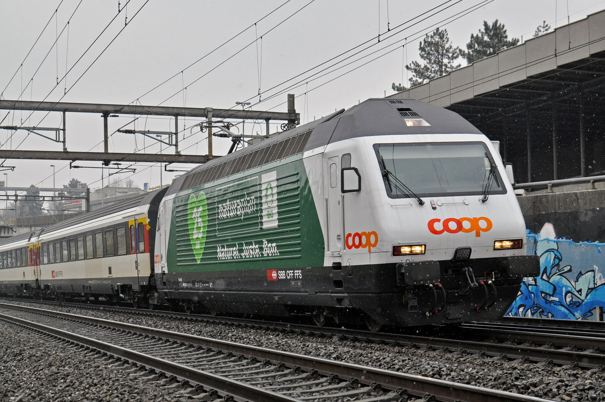 Re 460 001-1, mit der COOP Werbung für 25 Jahre Naturaplan, fährt bei leichtem Schneefall Richtung Bahnhof Muttenz. Die Aufnahme stammt vom 08.02.2018.