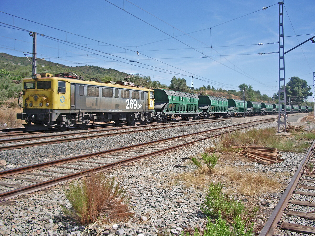 Samstag den 29.07.2006 um 12:41 Uhr in Botarell (Provinz Tarragona, Spanien). Güterzug mit Salz oder Kohle beladen im Bahnhof von Riudecanyes–Botarell (Spanien). Der Bahnhof liegt an der Bahnlinie Madrid – Reus – Barcelona. Als Zuglok dient die RENFE (Red Nacional de los Ferrocarriles Españoles / Nationales Netz der spanischen Eisenbahnen) Elektrolokomotive 269 071-7 (UIC-Nr. 91 71 2269 071-7); Baujahr: 1976, Baureihe: 269, Achsfolge: Bo’Bo’ (vier einzeln angetriebene Achsen), Stromsystem: 3'000 Volt Gleichstrom (3 kV =), Spurweite: 1’672mm (ursprüngliche Spanische Breitspur) / 1’668mm (heutige Iberische Breitspur), Erbauer: CAF (Construcciones y Auxiliar de Ferrocarriles). Dieser Güterzug führt vermutlich Kohle und nicht Salz da die Wagen grau verfärbt sind. Koordinaten GMS (Grad, Minuten, Sekunden): N 41° 8’ 22.3’’ O 0° 58’ 26.9’’