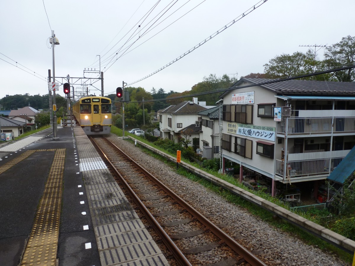 Seibu-Konzern, Tamako-Linie (Die Linie zum Tama-Stausee): Der Vierwagenzug 2533 ist den Berg heraufgekommen und fährt in die Endstation Seibu Yûenchi (Seibu Vergnügungspark) ein. Am Gebäude rechts im Bild hängt Werbung für die Büros darin - Werbung für ein Heiratsvermittlungsbüro (mit roten Herzchen für Frauen und blauen Herzchen für Männer), darunter für einen Liegenschaftsmakler / eine Liegenschaftsverwaltung, und am Balkon für die kommunistische Partei Japans. 22.Oktober 2011.  