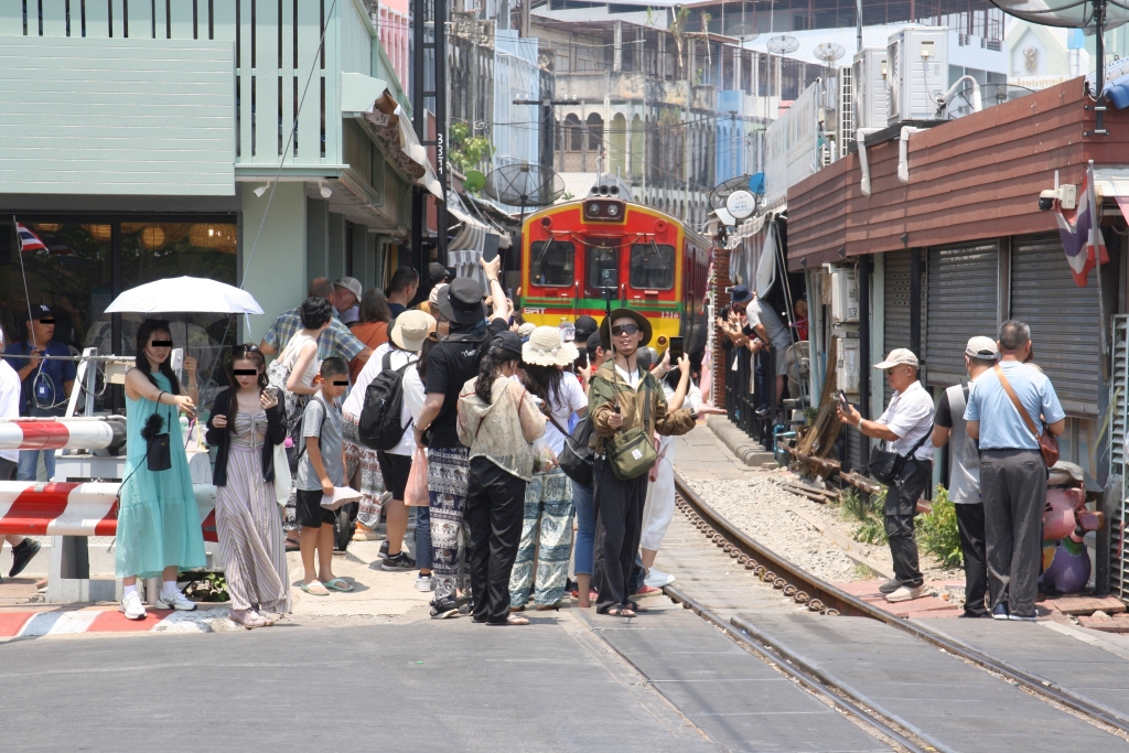 Seit sehr viele Reiseanbieter die Mae Klong Station mit dem gleich anschließenden Markt im Programm haben fahren die Züge dort nur mehr im Schritttempo, dabei sind wegen unachtsamer Fotografen (Idioten darf man ja nicht sagen) 2-4 Notbremsungen nichts außergewöhnliches mehr. - Im Bild vom 01.Mai 2024 kämpft sich der NKF 1216 als erstes Fahrzeug des ORD 4384 den Weg durch die Menschenmassen.