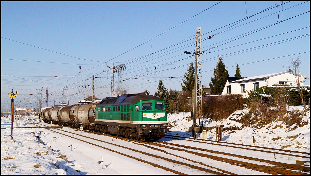 Sonne und etwas Neuschnee lockten mich am 06.02.2015 vor die Tür. Also erst mal los zum Abzweig Srg und die UBB und den RE 3  abarbeiten . 

Die Schranken schlossen sich erneut und die Lage der Weichen verriet, dass da was durch die Berliner Kurve fahren würde, aber was? Zum Spekulieren blieb keine Zeit, denn das immer lauter werdende Dieselgrummeln aus Richtung Rügen lies die Spannung steigen. 

Ein paar Augenblicke später fährt V300 003 mit einem leeren Getreidezug von Sassnitz-Mukran kommend in die KBS 203 ein und bringt etwas Grün in den Winter.