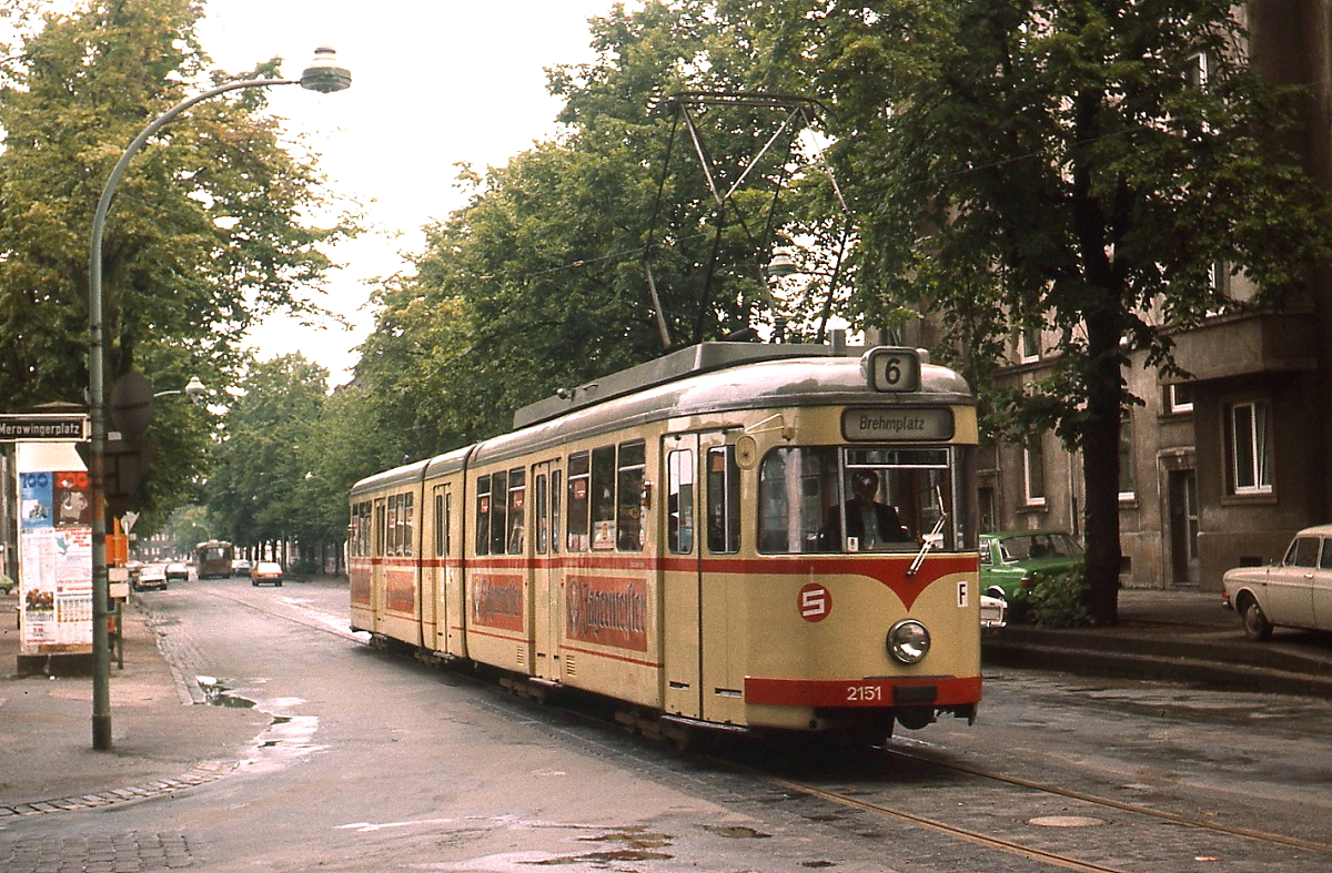 Um 1979 hält der Tw 2151 der Rheinbahn als Linie 6 an der Haltestelle Merowingerplatz. Nachdem sich die Verkehrsunternehmen im Rhein-Ruhr-Bereich zum VRR (Verkehrsverbund Rhein-Ruhr) zusammengeschlossen hatten, erhielten die dort verkehrenden Linien ab 01.06.1980 dreistellige Nummern. Den Düsseldorfer Linien wurde eine  7  vorgestellt und so wurde aus der  6  die  706 . Um Personal (Schaffner) einzusparen, baute die Rheinbahn den Großraumwagen 2020 und den Beiwagen 1604 unter Zufügung eines Mittelteils zum Gelenkwagen 2151 um. Wegen der laufenden Beschaffung von Gelenktriebwagen unterblieben weitere Umbauten und der wegen seiner Länge auch als  Queen Mary  bezeichnete Tw blieb ein Einzelstück. Das Fahrzeug ist museal erhalten.