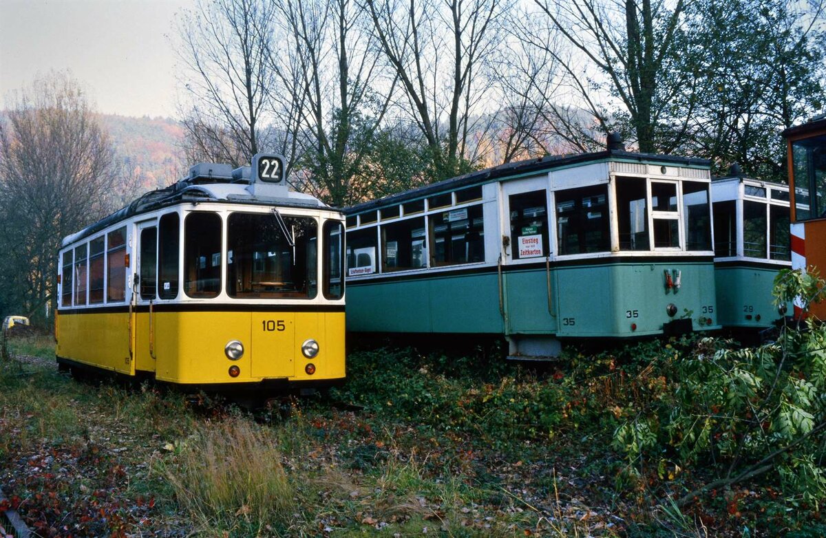 Vor dem Bahnhof Schönau der früheren DB-Bahnstrecke Neckarsteinach-Schönau wurden seit 1984 verschiedene erhaltenswerte Straßenbahnfahrzeuge abgestellt und sich selbst überlassen. Links abgestellt war TW 105 der Stuttgarter Zahnradbahn, rechts daneben die Beiwagen 35 und 29 der Überlandstraßenbahn Esslingen-Nellingen-Denkendorf. Sie sollten einst alle als historische Fahrzeuge auf dieser früheren DB-Bahnstrecke eingesetzt werden. Daraus wurde leider nichts. Das Foto entstand im Herbst 1984.