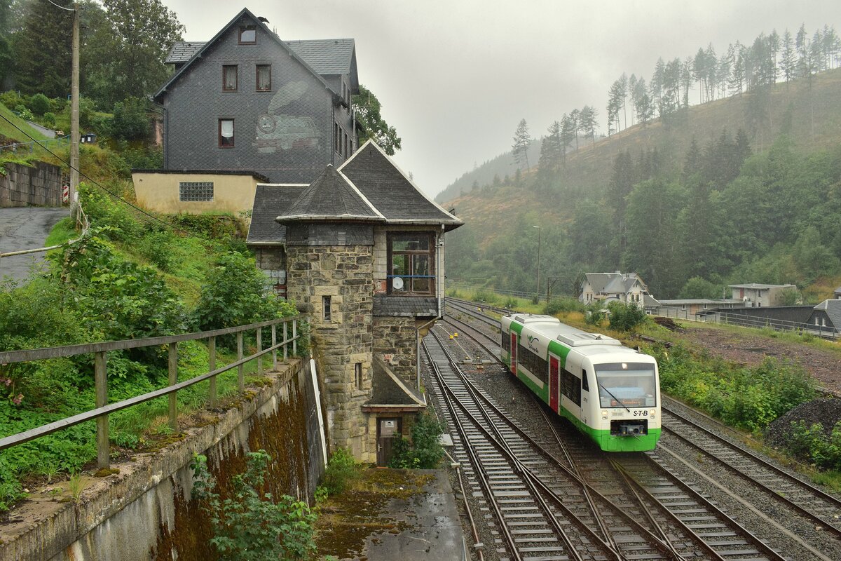 VT116 erreicht von Neuhaus am Rennsteig kommend im Nieselregen den Bahnhof Lauscha und passiert das alte Stellwerk. Das Stellwerk der Bauart Jüdel ging 1912 in Betrieb und wurde am 22.1.1997 außer Betrieb genommen und durch ein ESTW ersetzt. Das Gebäude ist verkauft und heute bewohnt oder anderweitig genutzt. Man beachte zudem das Dampflok Motiv an der Häuserwand. Das Bild wurde von einem Fußgängerweg aus aufgenommen.

Lauscha 02.08.2023