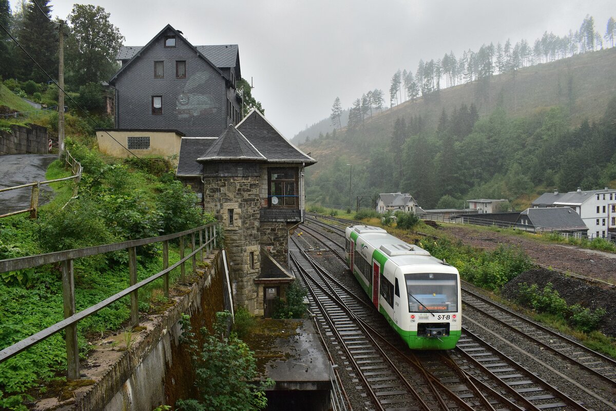 VT129 verlässt im Nieselregen den Bahnhof Lauscha in Richtung Neuhaus am Rennsteig und passiert das alte Stellwerk. Das Stellwerk der Bauart Jüdel ging 1912 in Betrieb und wurde am 22.1.1997 außer Betrieb genommen und durch ein ESTW ersetzt. Das Gebäude ist verkauft und heute bewohnt oder anderweitig genutzt. Man beachte zudem das Dampflok Motiv an der Häuserwand. Das Bild wurde von einem Fußgängerweg aus aufgenommen. 

Lauscha 02.08.2023