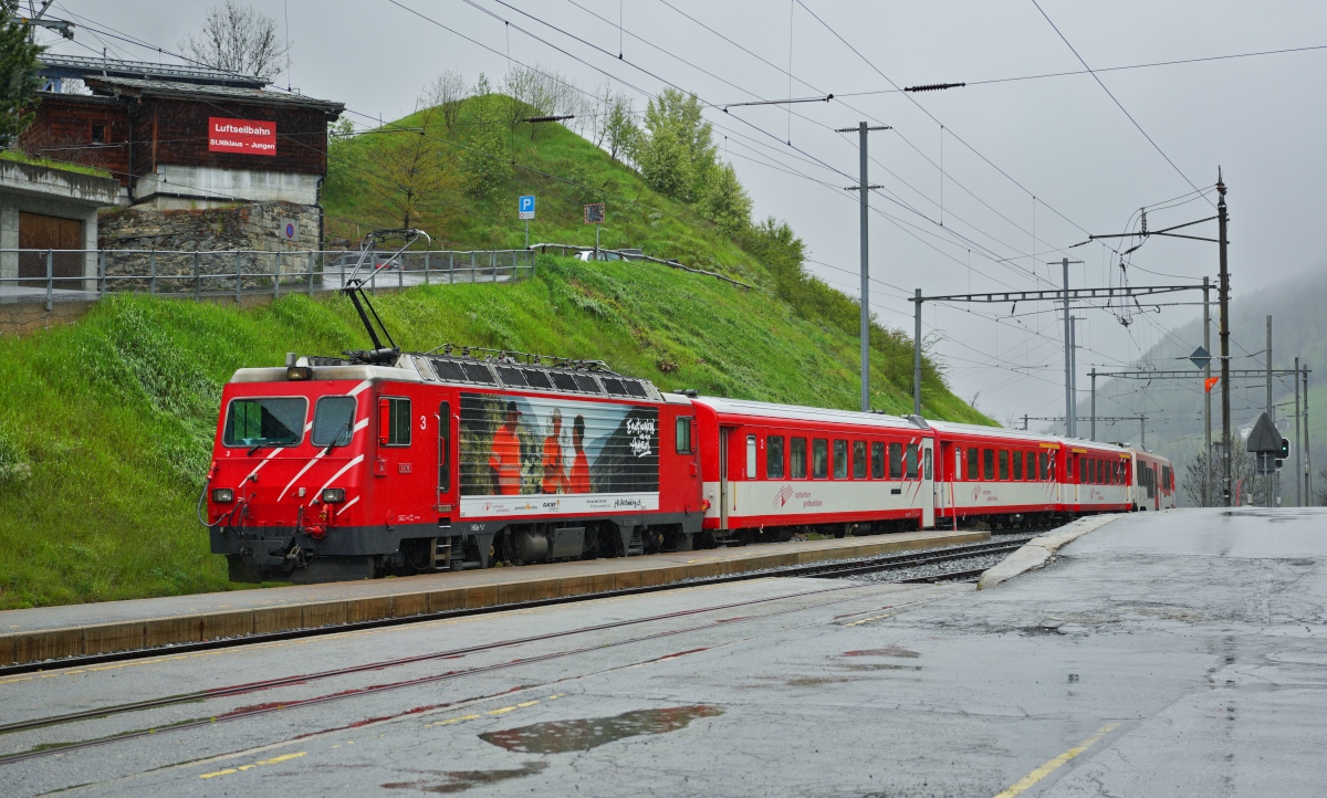 Während die von der Furka-Oberalp-Bahn beschafften HGe 4/4 II 101-108 und die frühere HGe 4/4 II 1 (jetzt 109) der Brig-Visp-Zermatt-Bahn einer umfassenden Modernisierung unterzogen wurden, unterblieb dies bei den weiteren von der Brig-Visp-Zermatt-Bahn beschafften Lokomotiven. Hierzu gehört die HGe 4/4 II 3, die am 07.05.2024 einen RE nach Visp aus dem Bahnhof St. Niklaus schiebt. Oberhalb der Lok die Talstation der Luftseilbahn St. Niklaus - Jungen, die in die 840 m höher gelegene gleichnamige Ortschaft führt.