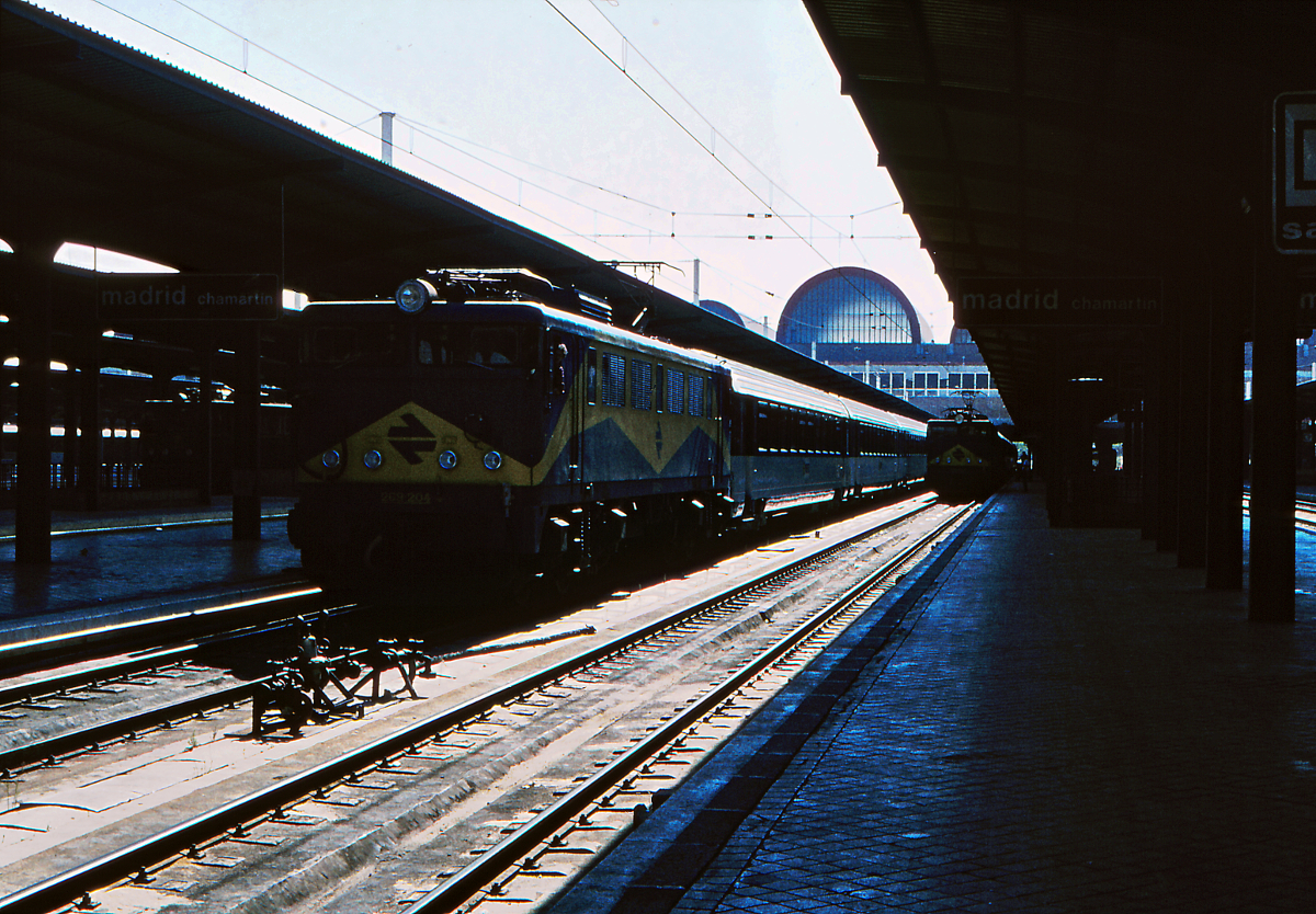 Zur Fußball-Weltmeisterschaft des Jahres 1982 wollte sich die Renfe modern präsentieren. Am Bahnhof Madrid Chamartin steht die damals neue 269 204 mit einem Rapido Corail nach Gijon bereit. Die Lokomotive wurde 1980 von CAF geliefert, das Farbschema und die Lok werden nach dem Designer  Mazinger  genannt. Die Waggons sind von der SNCF angemietet und führen zur Bestellung der (damals) modernen Serie 9000 der Renfe. Oktober 1981.
Canon AE1, Canoscan, GIMP.   