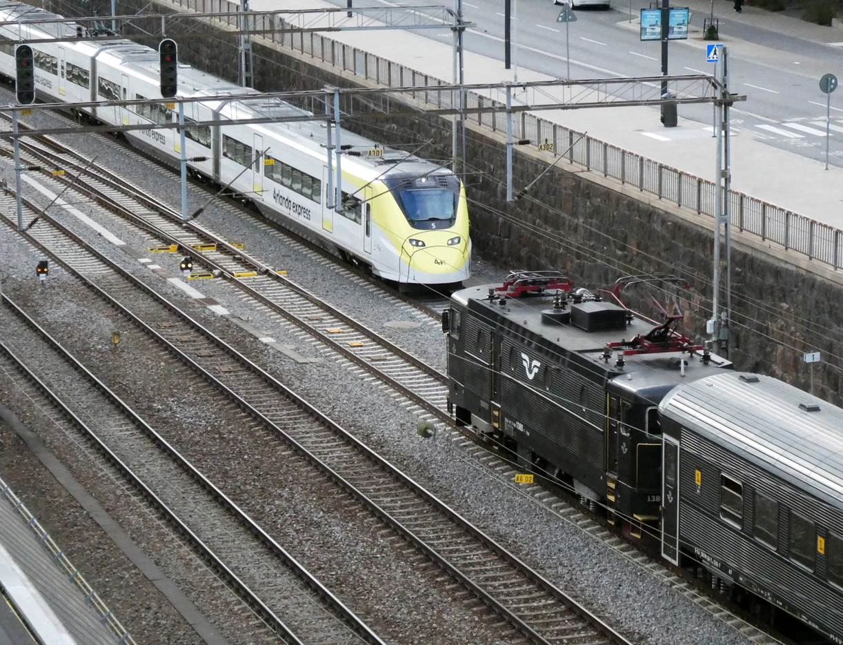 Der Arlanda-Express von und nach dem Flughafen begegnet einer Rc3 im Gleisfeld nördlich des Bahnhofs Stockholm C., fotografiert von einer Strassenbrücke. Stockholm, 5.8.2024