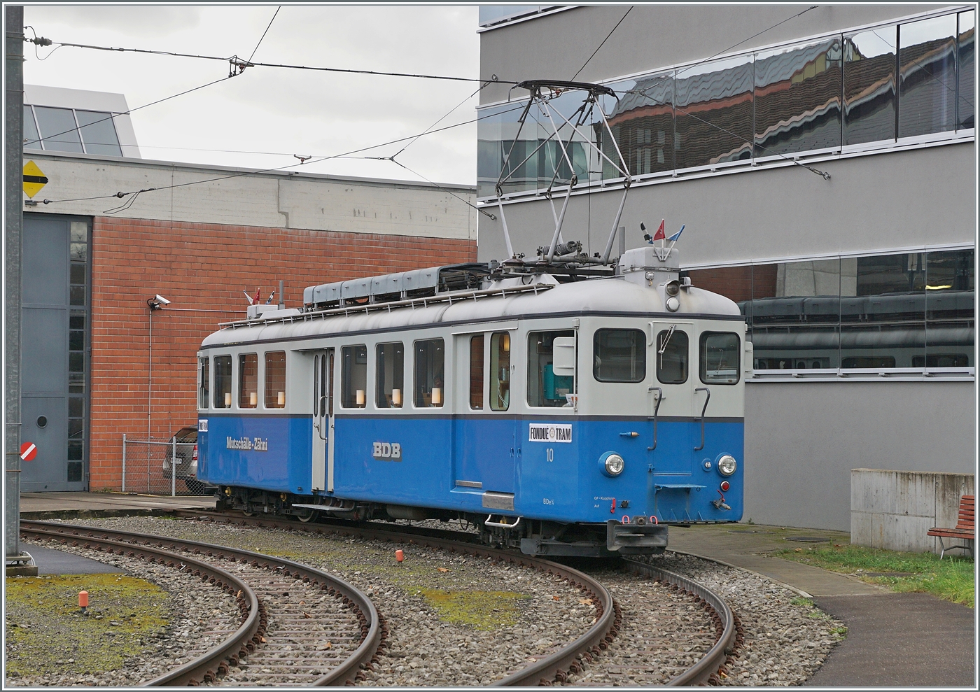 Der BDe 4/4 10 wurde im Jahre 1928 in Betrieb genommen. Gebaut hat dieser Triebwagen die Schweizerischen Wagonfabrik in Schlieren und die Maschinenfabrik Oerlikon, beide Werke sind nicht weit von der Bremgarten Dietikon Bahn entfernt im Limmattal bzw. bei Zürich. Der 16.22 Meter lange, 32 Tonnen schwere und 45 Km/h schnelle Triebwagen stand mit seinem Schwesterfahrzeug BDe 4/4 11 bis 1986 bei der BD im Einsatz. Während der BDe 4/4 11 mittlerweile ausrangiert wurde, konnte der BDe 4/4 10 zum Gesellschaftswagen umgebaut werden. Der heute als  Mutschälle-Zähni  im Sonderzug Einsatz stehende Triebwagen bietet in vielerlei Hinsicht einen geschätzten Beitrag im exklusiven Nostalgieverkehr und einen interessanten Gegenstz zum Planverkehr. Heute wartet das  Mutschälle-Zähni  auf den Einsatz als  Fondue-Tram  im Rahmen des bekannten Weihnachtsmarkts von Bremgarten.
(Fotostandpunkt: auf dem Bahnsteig)
6. Dez. 2024