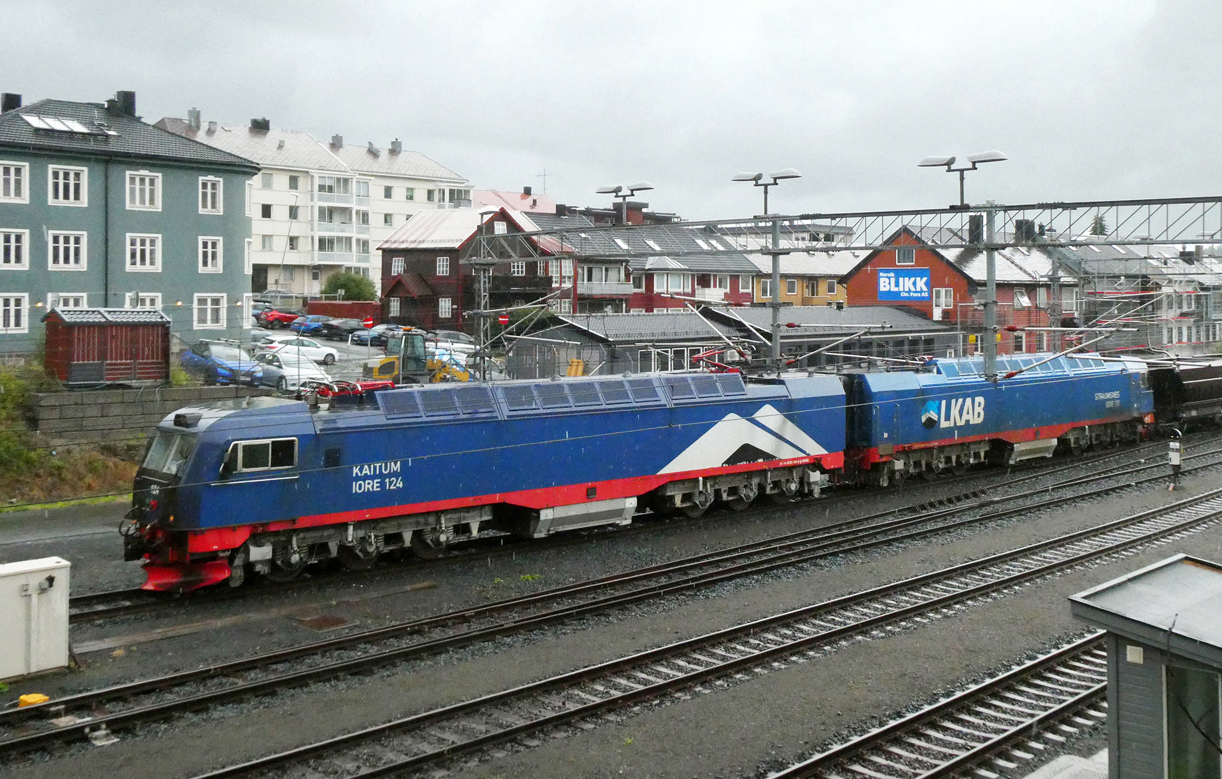 Doppellok 124 fährt mit ihrem beladenen Erzzug aus Kiruna im Regen zur LKAB-Abladestation. Das Foto wurde von einer Strassenüberführung aus gemacht. Narvik, 16.8.2024