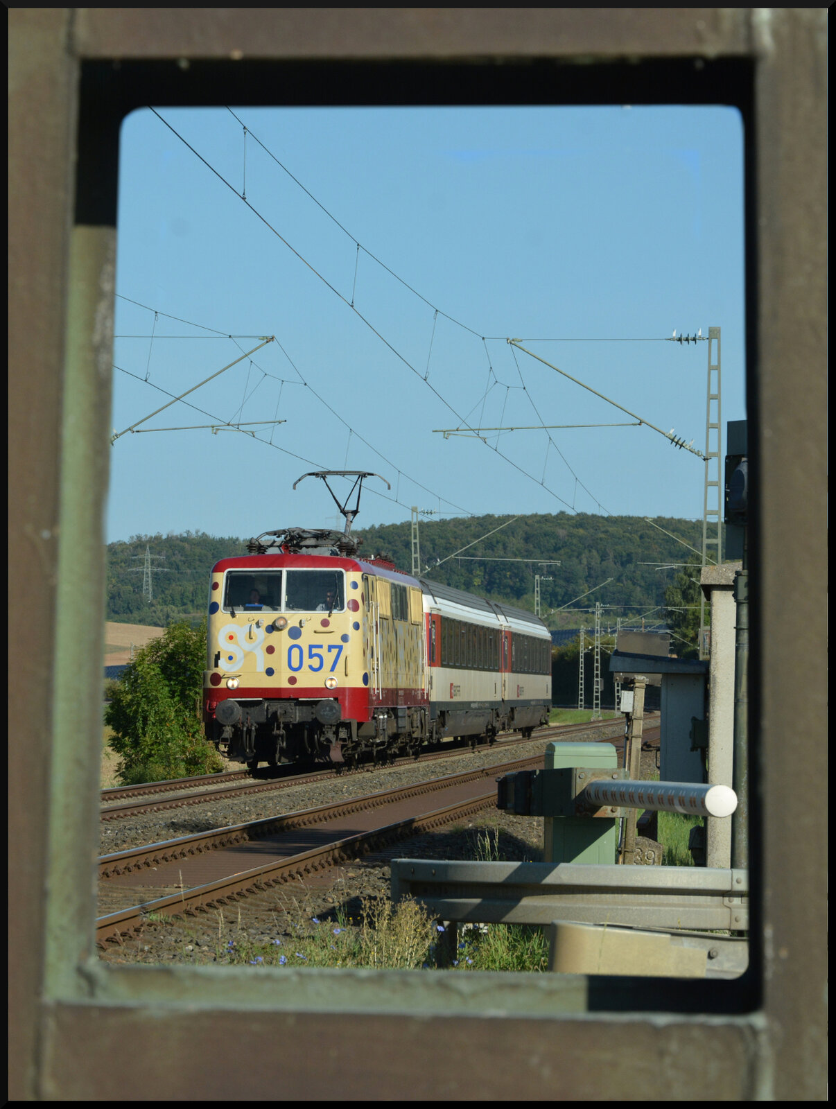 Durchblick: Am 27.08.2024 überführte 111 057 (Baujahr 1974, smart rail GmbH, 91 80 6 111 057-6 D-Zug), hier beim Weiler Moos, zwei schweizerische Reisezugwagen (SBB, Bmpz) von Basel über Heilbronn und Würzburg nach Fulda. Die SBB-Wagen gingen von dort weiter nach Halberstadt zur Revision und Modernisierung bei VIS Verkehrs Industrie Systeme GmbH.