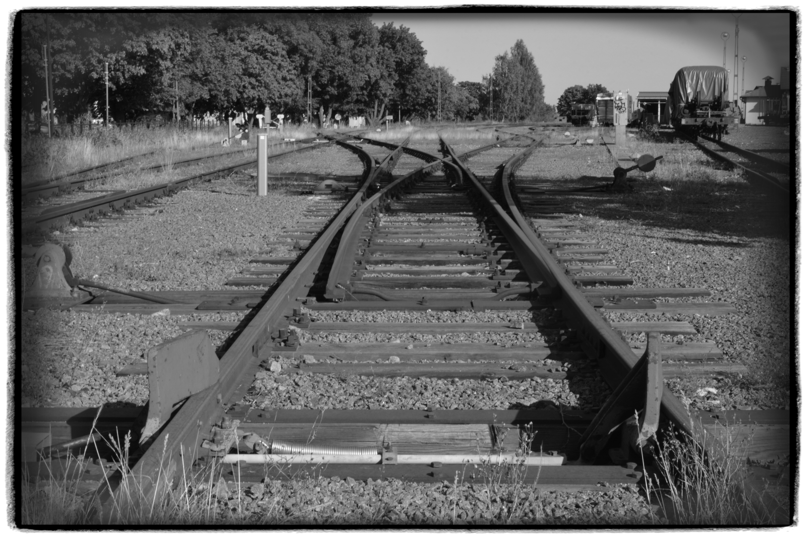 Eine Dreiwegeweiche im Normalspurteil des Bahnhofs Västervik. Die umfangreichen Gleisanlagen sind seit Jahren verwaist. Links zweigt der Anschluss zum Hafen der Stadt ab. Dorthin sind auch schon lange keine Züge mehr rangiert worden. Rechts befinden sich die Schmalspurgleise (Spurweite: 891 mm) der Smalspåret Västervik - Hultsfred. HINWEIS: Das Foto entstand am 19.08.2024 vom geöffneten BÜ aus.