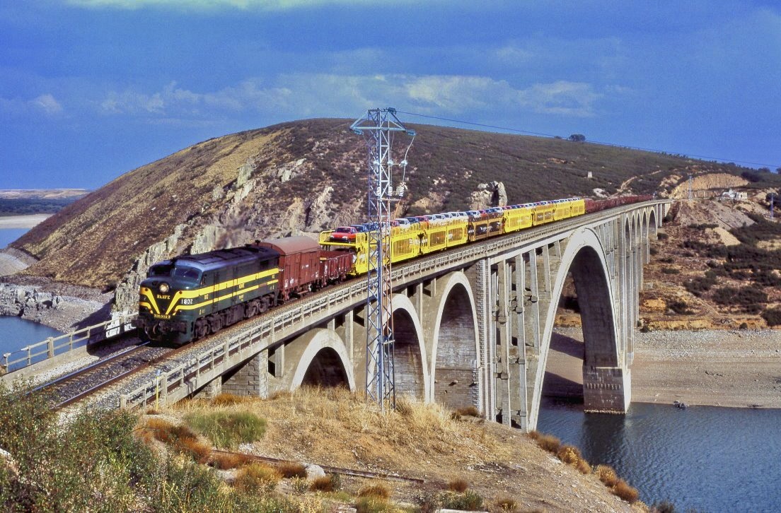 Embalse del Esla de Ricobayo nennt sich die Talsperre im Nordwesten Spaniens. Hier wird der Esla, ein Nebenfluss des Duero groflchig aufgestaut. Die Bahnstrecke Madrid - A Corua im Abschnitt Zamora - Ourense berquert diesen auf einer 1942 gebauten Betonbrcke mit einer Bogenspannweite von 208m (lange Jahre Weltrekord). So interessant wie die Brcke ist auch die Lok: die Baureihe 318 (ALCo DL-500C) wurde in 24 Einheiten beschafft und von 1955 bis 1994 eingesetzt. 318 002 war am 16.09.1990 bei Manzanal mit eine Zug nach A Corua unterwegs.
