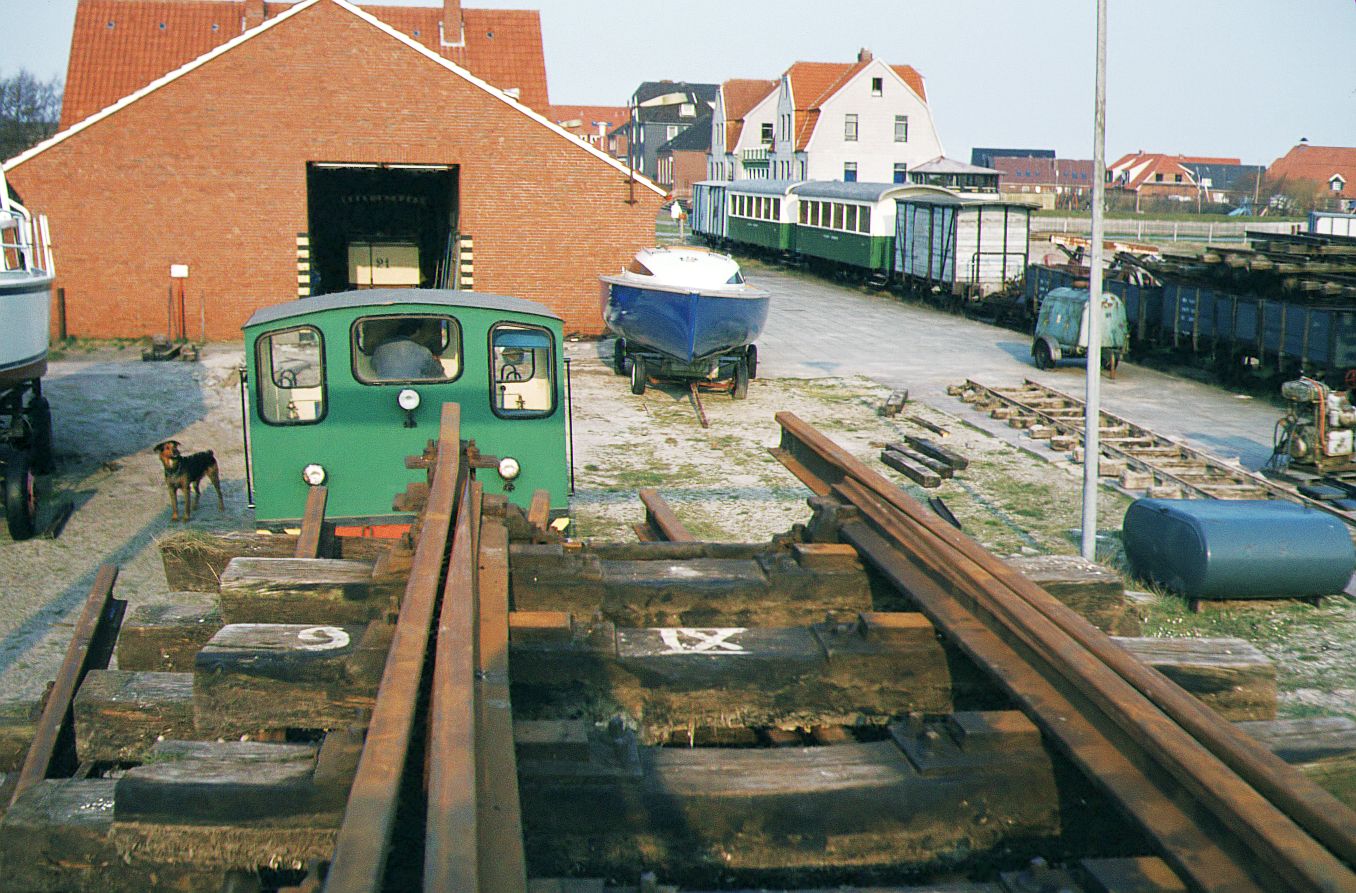 Inselbahn Spiekeroog__April 1984.Ehemaliges Bahnhofsgelände Spiekeroog. Über die SCHÖMA-Lok 4 hinweg ist in der Halle der Pferdebahnwagen 21 aus Stuttgart zu sehen. Noch ist keine Saison für die Pferdebahn. (Allerdings verzögerte sich die Betriebsaufnahme in dieser 4. Saison durch kurzfristig angekündigte <identische...> kräftige Preiserhöhungen bei beiden involvierten Reitstallbetrieben für die Pferdegestellung, worauf durch Anschaffung eines eigenes Pferdes die Lösung für einen kostendeckenden Weiterbetrieb gefunden wurde).