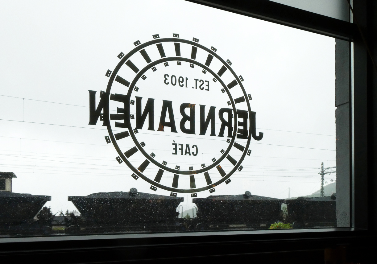 Währenddem wir im warmen Bahnhofscafé in Narvik bei einem Kaffee das Jernbanen-Logo an der Fensterscheibe bewunderten, rollte draussen im Regen ein Erzzug Richtung LKAB-Abladestation vorbei. Narvik, 16.8.2024