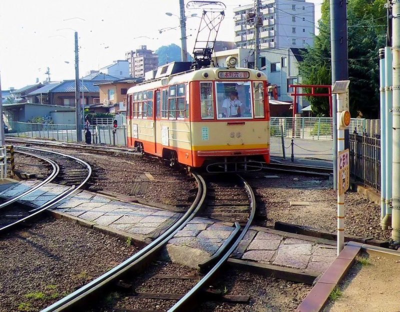 Matsuyama Strassenbahn, Serie 62-69: Diese leichten Wagen wurden 1960/62 in der damaligen Busbautechnik erstellt und haben gesickte Seitenwnde.  Im Gegensatz zur Serie 51-61 (15,88 t) wiegen sie nur 12,96 t. Wagen 68 kommt soeben aus der Abstellanlage der Endstation Dgo Onsen zurck, wo er das Gleis gewechselt hat. Rechts vom Wagen im Hintergrund sieht man das rote Tor zu einem kleinen Gtterschrein. 17.September 2009. 