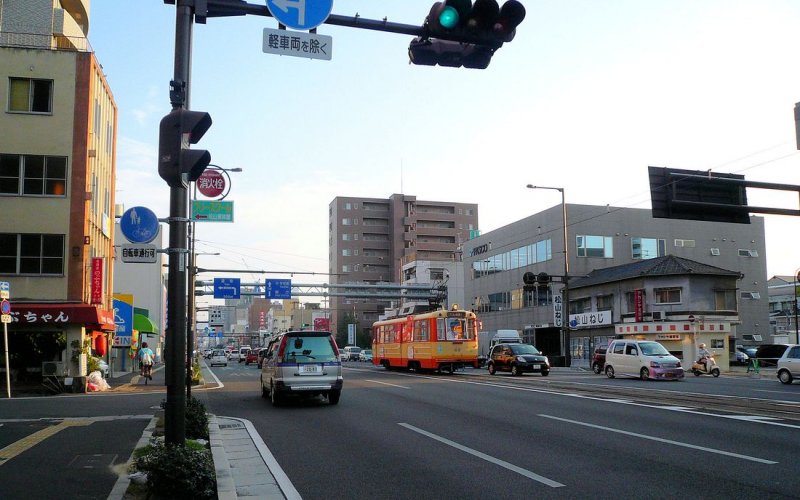 Matsuyama Strassenbahn, Serie 62-69: In den letzten Strahlen der Abendsonne befhrt Wagen 68 eine einspurige Querverbindungsstrecke. Als die Insel Shikoku nur ber die Fhre zu erreichen war, gab es noch keine solchen grossen Strassen. Honch Gochme, 17.September 2009. 