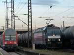 185 566 der MRCE CFL Cargo schiebt sich mit ihrem Kesselwagenzug zwischen die wartende Regionalbahn.