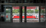 Draußen im Bahnhof eine rote Lok -    Blick durch den Innenhof eines Bürohauses auf den Stuttgart Hauptbahnhof, wo sich gerade ein IC-Zug in Bewegung setzt.