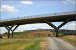 Bahnbild ohne Bahn und Schienen - 

Diese Brücke wurde schon vorsorglich für das Bahnprojekt Stuttgart 21 bzw. die SFS Stuttgart - Ulm mitgebaut, da im Rahmen des Messeneubaus eine Straßenbrücke über die Autobahn A8 verlegt werden musste.
Die Bahntrasse soll hier vier Gleise haben, in der Mitte die Strecke von und nach Ulm während rechts und links die Gleise der Gäubahn nach Horb in abgesenkter Rampenlage. Die Gäubahn wird im Rahmen dieses Bahnprojektes nicht mehr die bisherige wunderschöne Stadteinfahrt nach Stuttgart nutzen, sondern ab Rohr über die S-Bahnstrecke zum Flughafen führen und dann in diesem Bereich mit einer engen 180° Kurve an die SFS in Richtung Stuttgart angeschlossen. Kurz vor dieser Brücke kommen die Züge der Gäubahn aus dem Flughafentunnel. Die Züge der Schnellfahrstrecke werden das im Hintergrund sichtbare Parkhaus unterfahren. Siehe auch: http://www.staedte-fotos.de/name/einzelbild/number/3945/kategorie/Deutschland~Baden-W%FCrttemberg~Stuttgart.html Noch ist aber der Bau dieses Projektes nicht entschieden. 

24.6.2007 (M)