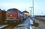 In Aulendorf wartet die 215 130-6 mit zwei Umbau-Vierachsern am 14.02.1983 auf die Abfahrt. Wie man zwischen Lok und erstem Wagen erkennen kann, arbeitet die Dampfheizung an diesem kalten Wintertag.