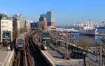 Blick auf die Station Landungsbrücken mit U-Bahn, Elbphilharmonie und Schiffen.