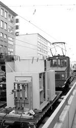 SSB Stuttgart__Arbeitsfahrzeuge der SSB in den 70er und 80er Jahren. A-Lok 2025 [ME/BBC 1946; Vk 1984 an Straßenb.Würzburg] mit 3 beladenen Flachwagen in der Schloßstr.  taucht  rückwärts ab in die Tunnelrampe (für die Linien 9 + 14) zur Baustelle Richtung Hbf. Ob die drei Buchstaben der Leuchtreklame zu der Ladung passen, kann ich nicht sagen...__08-01-1976