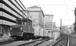 SSB Stuttgart__Arbeitsfahrzeuge der SSB in den 70er und 80er Jahren. A-Lok 2025 [ME/BBC 1946; Vk 1984 an Straßenb.Würzburg] mit 3 beladenen Flachwagen in der Schloßstr.  taucht  rückwärts ab in die Tunnelrampe (für die Linien 9 + 14) zur Baustelle Richtung Hbf.__08-01-1976