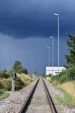 Dunkle Wolken über der Thüringer Oberlandbahn. Blick vom Bahnübergang am Bahnhof auf die Reste der Thüringer Oberlandbahn von Ebersdorf Friesau aus. Das Gleis endet ein paar Meter hinter dem Bogen und wird heute als Ausziehgleis genutzt. Heute fahren hier jedoch nur noch Holzzüge nach Ebersdorf-Friesau zum Sägewerk. Ab dem Sägewerk ist die Strecke noch ein paar Meter befahrbar ehe eine Sh2 Scheibe den Weg versperrt. Der Personenverkehr wurde am 24. Mai 1998 eingestellt und der Güterverkehr wenige Monate später auf dem Abschnitt Triptis - Ebersbach Friesau Ende 1998. Seit dem 1.1.2005 ist die Strecke Triptis - Ebersbach Friesau offiziell stillgelegt.

Ebersdorf Friesau 01.08.2023