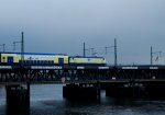 Himmel, Eisenbahnbrcke und Wolken sind zu sehen, Wind, Schiffe und Lagerhuser nicht.