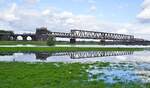 Am 12.10.2024 spiegelt sich eine Railpool-186 mit der Duisburg-Hochfelder Hochbrücke in einer überschwemmten Wiese auf der Rheinhausener Seite