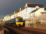 Regionalzug nach Exeter fährt in der Morgensonne vor einer schönen Häuserzeile bei Dawlish nordwärts. Dawlish, 18.5.2022