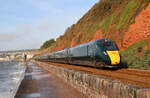 Auch vom Fussweg aus gelingen gute Fotos: Schnellzug zwischen Dawlish und Dawlish Warren auf dem Weg Richtung Norden in der Morgensonne. Links im Hintergrund ist die bei den Fotografen beliebte Fussgängerüberführung zu sehen. Dawlish, 18.5.2022